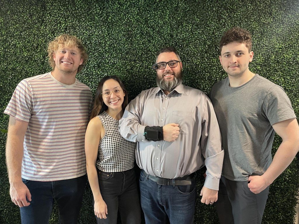 Jack, Gabby, Bryan, and Marley standing together in front of a plant covered wall showing off the AlEye system.